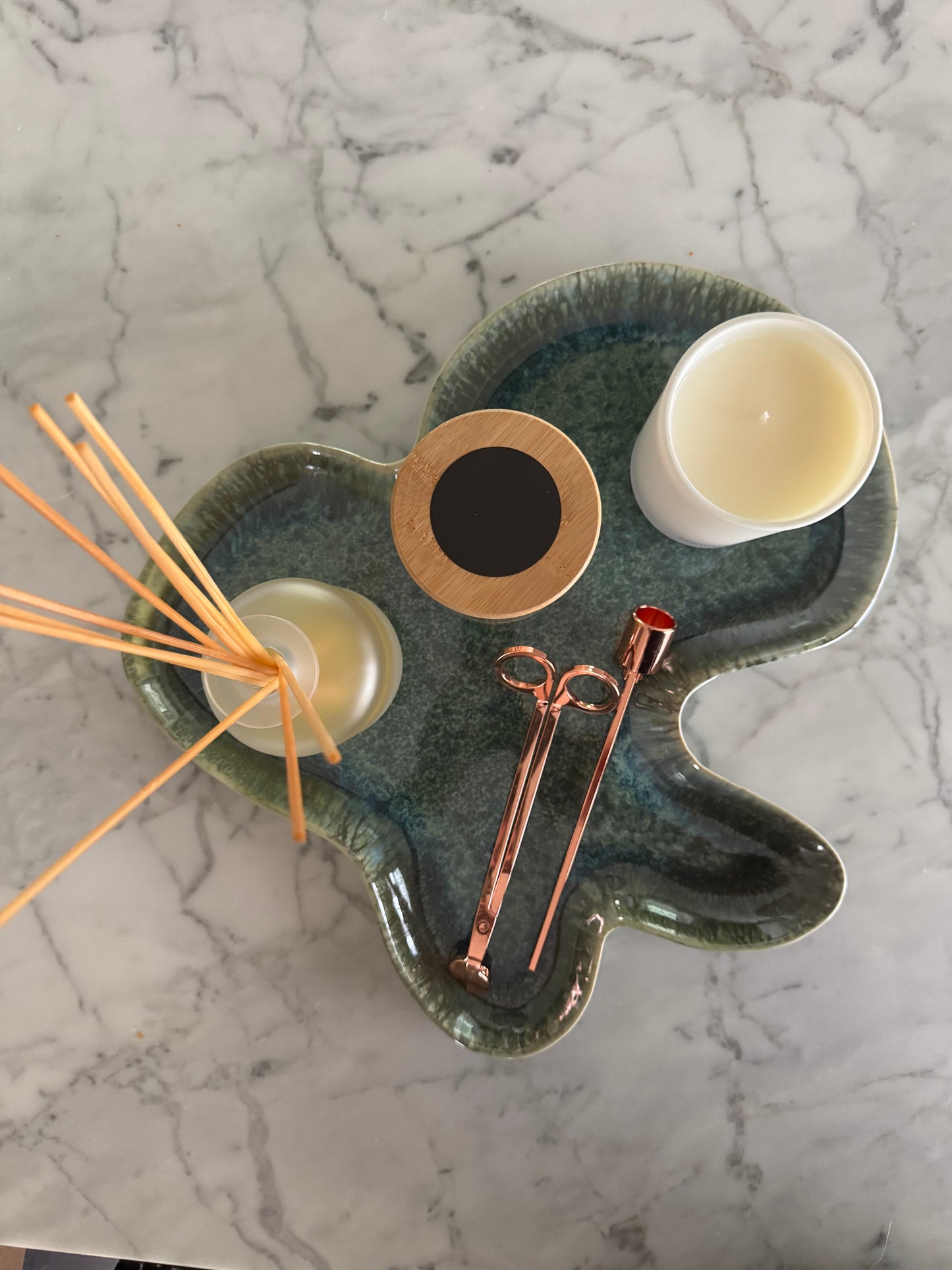 Ceramic tray with candles, wick trimmers, and wooden sticks on a marble surface