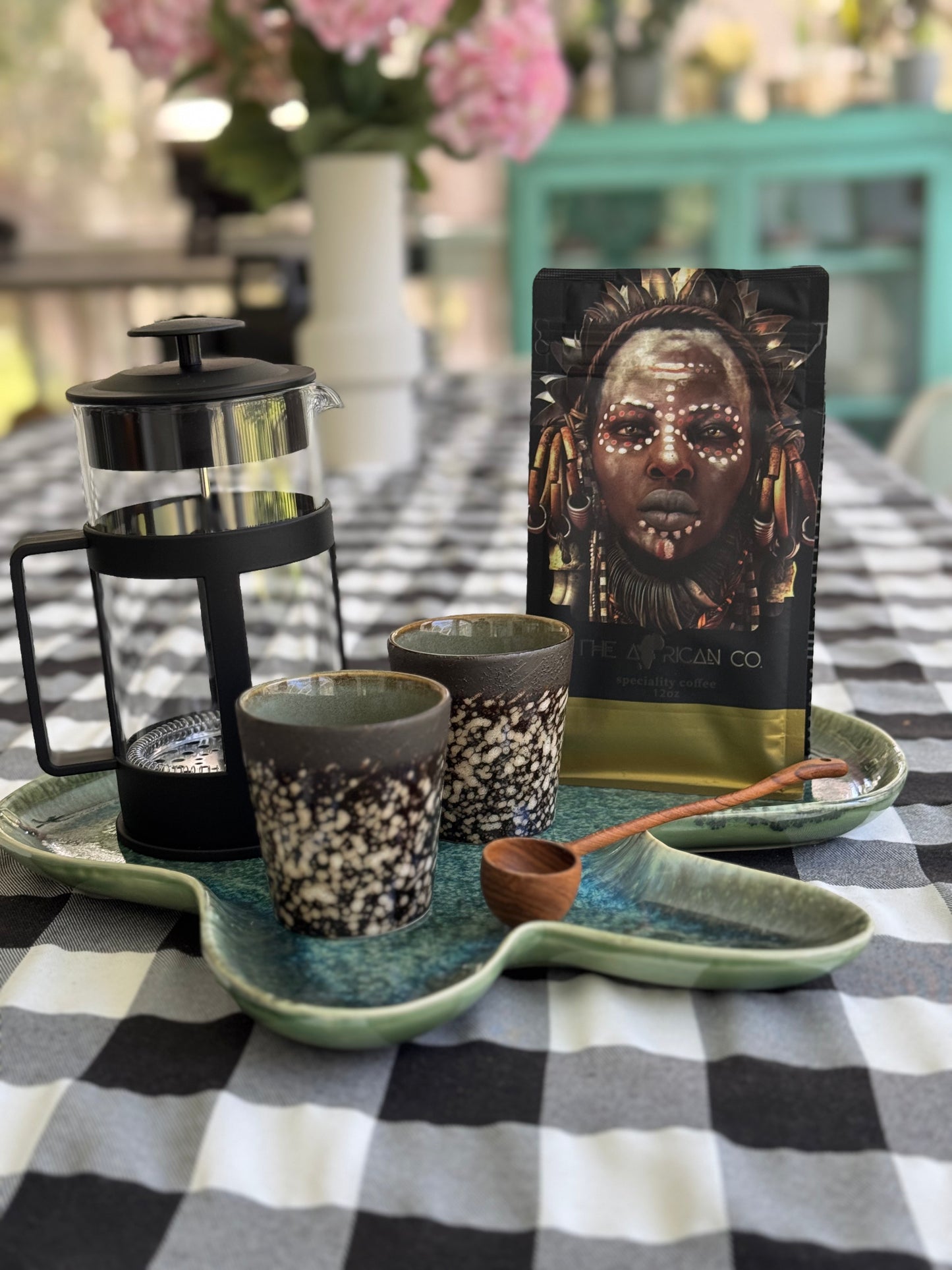 Café au Lait coffee package with a French press, mugs, and a tray on a checkered tablecloth.