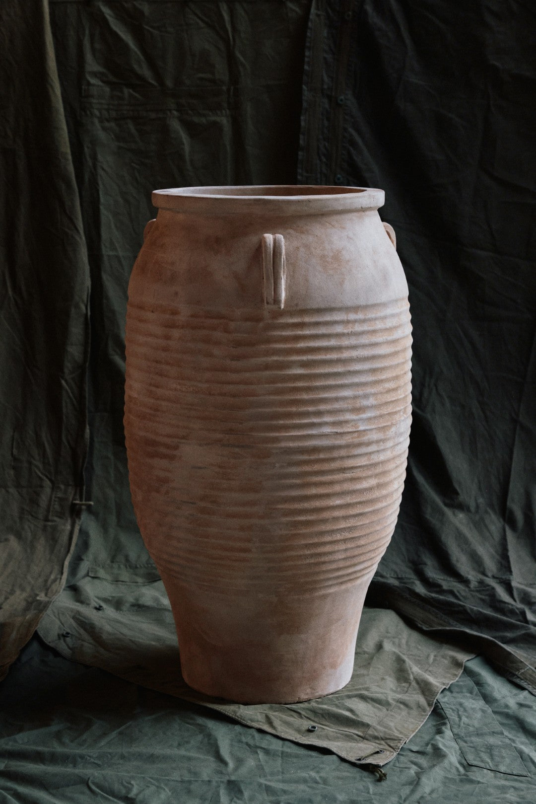 Large terracotta vase with ribbed texture on a dark green fabric background