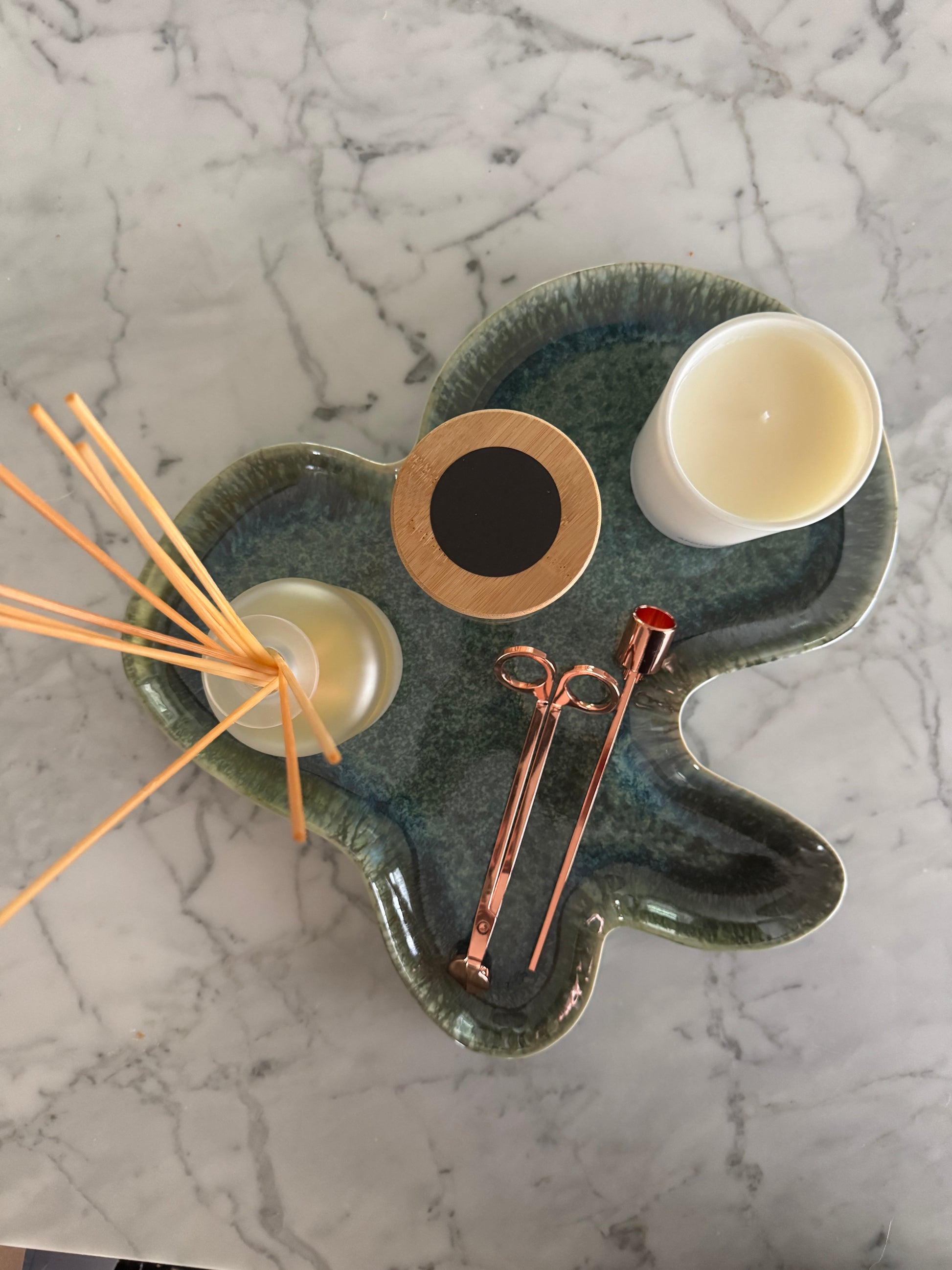 Ceramic tray with candles, wick trimmers, and wooden sticks on a marble surface