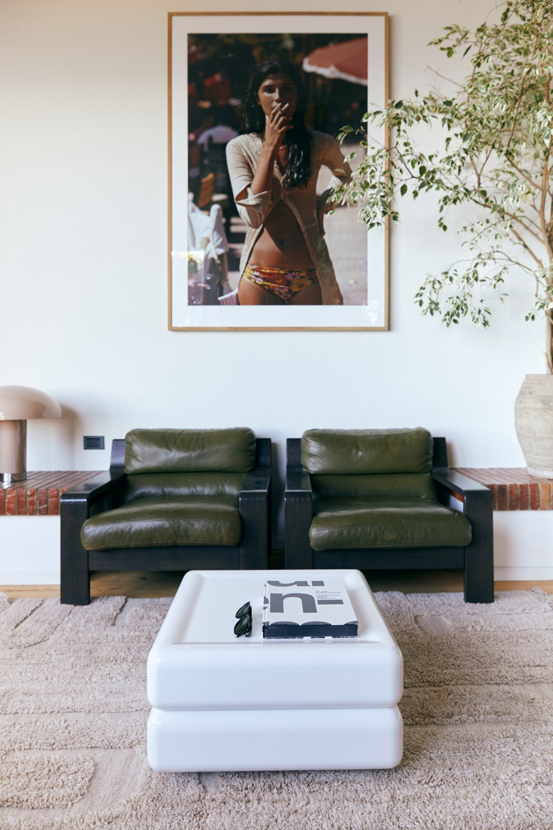 Modern living room with olive green leather sofas, a white ottoman, and framed artwork on the wall.