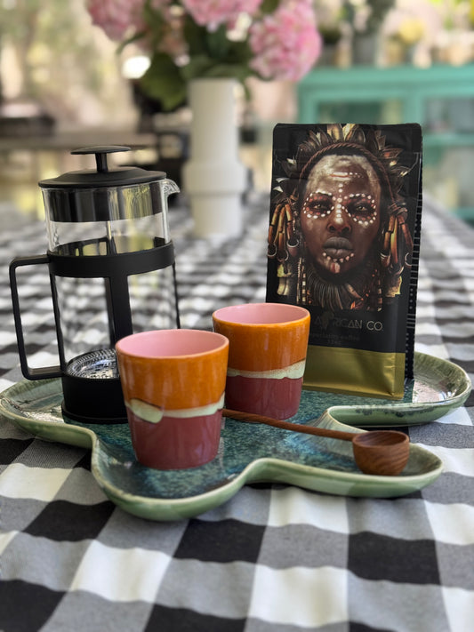 Café items including a French press, mugs, and a coffee bag on a checkered tablecloth.