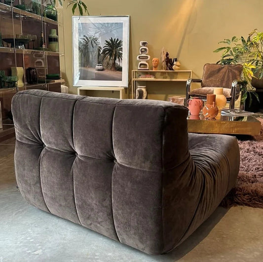 Gray tufted sofa in a living room with decorative items and plants.