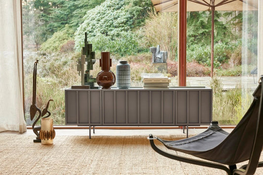 Modern living room with a long dark gray console table against a large window with greenery outside.