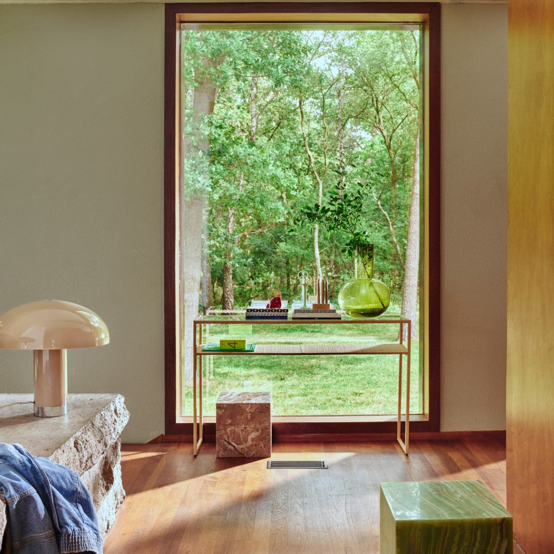 Modern interior with a large window view of trees, a table with decorative items, and a lamp.