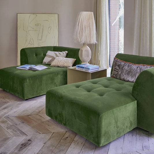 Green sofa in a living room with a lamp and books on a wooden floor.