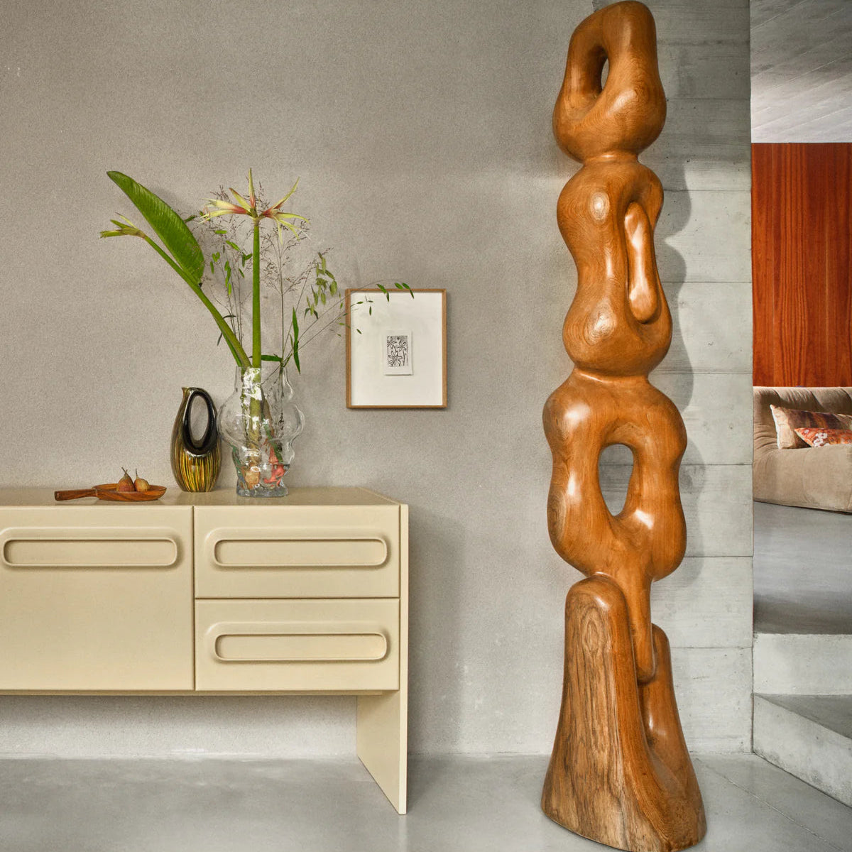 Wooden sculpture in a modern interior setting with a sideboard and decorative items.