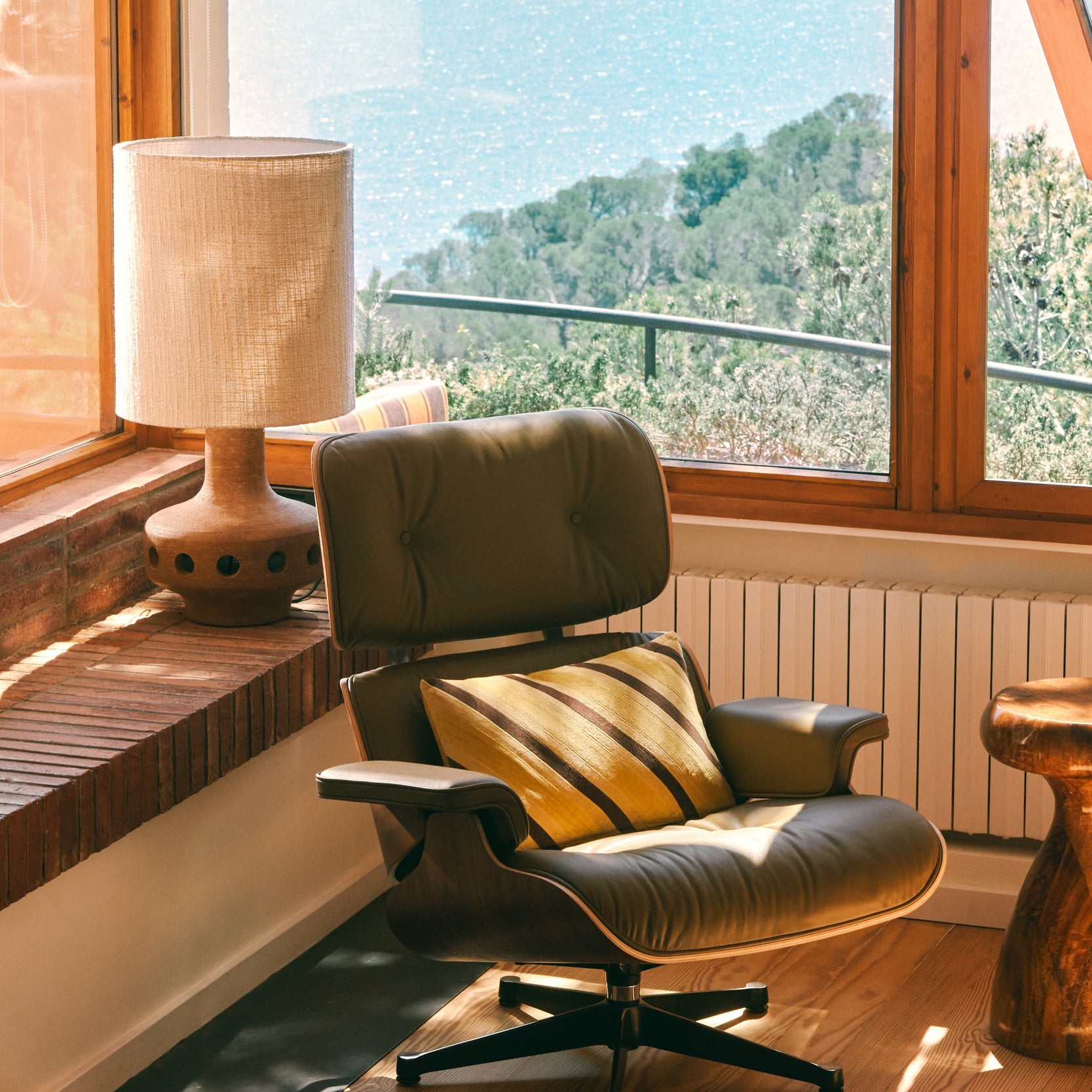 Modern chair with a cushion in a room with large windows offering a view of trees.