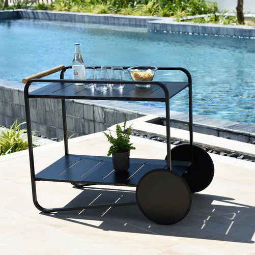 Black metal serving cart with a glass top by a poolside
